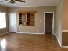 an empty living room with hard wood floors and ceiling fan in the corner, looking into the dining area