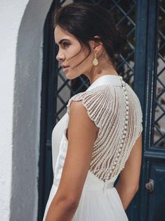 a woman in a white dress standing next to a blue door and wearing pearls on her back