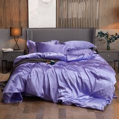 a bed with purple sheets and pillows in a living room next to a painting on the wall