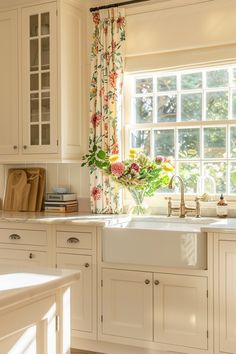 a kitchen with white cabinets and flowers on the window sill in front of the sink