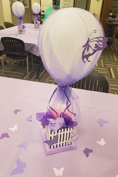 a table topped with a basket filled with purple flowers and balloons in the shape of a balloon