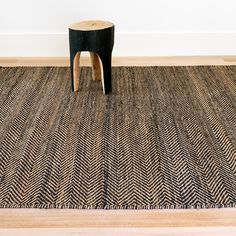 a black and white rug with a wooden stool on the floor in front of it