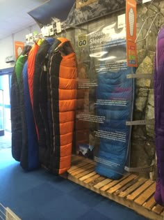 an assortment of sleeping bags on display in a store with blue carpet and stone walls