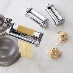 two pasta cutters and three uncooked noodles on a white counter with silver faucet