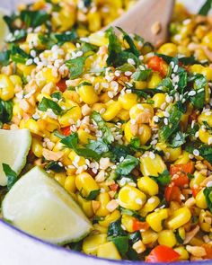 a bowl filled with corn and garnish next to a wooden spoon