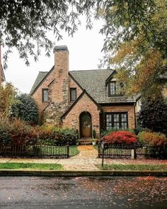 a brick house with trees and bushes in the front yard, on a rainy day