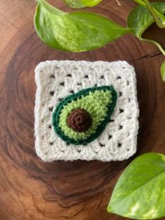 a crocheted square with a green eye on it sitting next to a plant