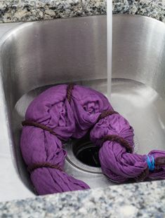 purple balls of yarn in a stainless steel sink with water running from the faucet