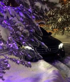 a car is parked in the snow next to a tree with purple lights on it