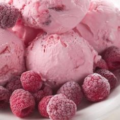 three scoops of ice cream with raspberries in a white bowl on a table