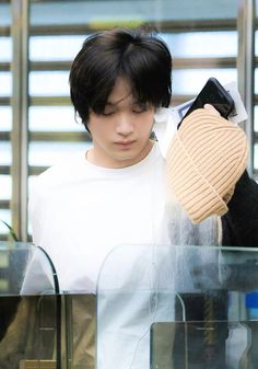 a young man with black hair and white shirt looking at something in a glass case