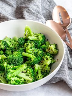 a white bowl filled with broccoli on top of a table next to a spoon