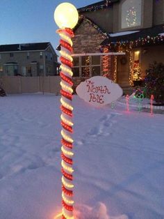 a lighted pole in the middle of a snow covered yard with christmas lights on it