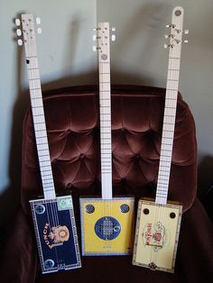 three guitars sitting on top of a brown chair next to two small boxes with magnets in them