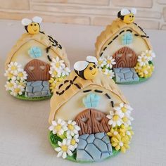 three decorated cookies with bees and flowers on top of a table next to a brick wall