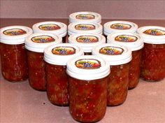 twelve jars of pickled fruit sit on a counter top in front of the camera