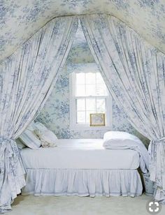 a white bed sitting next to a window in a room with curtains on the windowsill