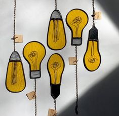 several yellow light bulbs hanging from chains with tags attached to them and pinned to the wall