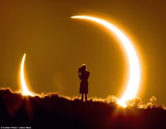 a man standing on top of a hill next to two eclipses in the sky