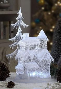 an ice sculpture of a house with snow on the roof and christmas trees in the background