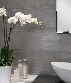 a white sink sitting under a mirror next to a vase with flowers in it on top of a counter