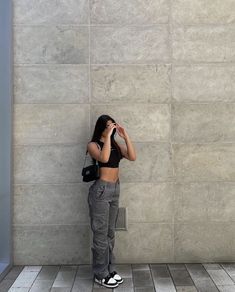 a woman standing in front of a wall talking on a cell phone with her hand to her face