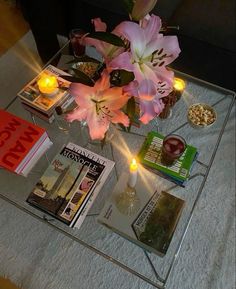 a glass coffee table topped with magazines and flowers on top of a white carpeted floor