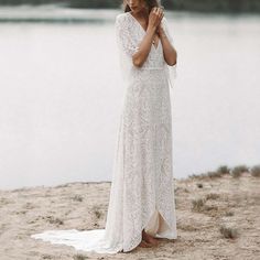 a woman in a white dress is standing on the beach and looking at the water