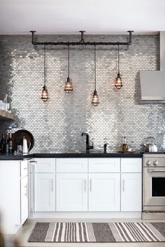 a kitchen with white cabinets and black counter tops, lights hanging from the ceiling over the stove