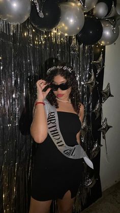 a woman in a black dress is posing for the camera with balloons and streamers behind her