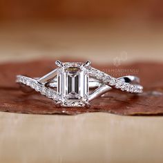 an emerald cut diamond ring on top of a brown leaf with diamonds surrounding it and the band