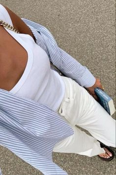 a woman wearing white pants and a blue striped shirt is looking down at her cell phone