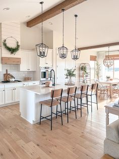 a large kitchen with white cabinets and wooden floors is pictured in this image, there are many chairs around the island