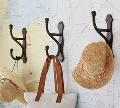 two hats hanging from hooks on a wall next to a bag and hat rack in front of a map