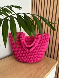 a pink crocheted bag sitting on top of a wooden table next to a plant