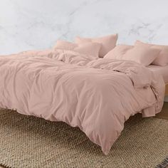 a bed with pink sheets and pillows on top of it in a room next to a rug