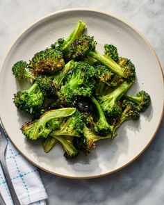 a white plate topped with cooked broccoli on top of a blue and white towel