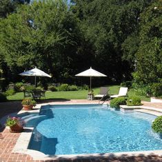 an empty swimming pool surrounded by trees and lawn chairs with umbrellas on the side