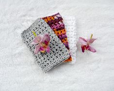 two crocheted bags with flowers on them sitting next to each other in the middle of a white blanket