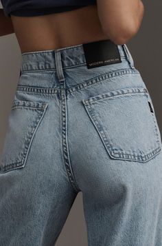 a woman in jeans is holding her cell phone up to her waist and looking down