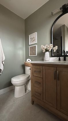 a white toilet sitting next to a wooden cabinet in a bathroom under a large mirror