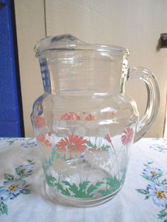 a glass pitcher sitting on top of a table next to a blue door with flowers painted on it