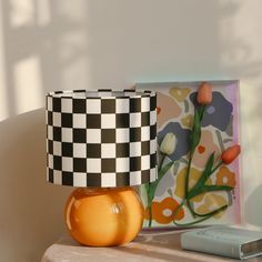 an orange vase sitting on top of a table next to a checkered lamp shade