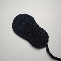 a black crochet hat with a string attached to it on a white surface