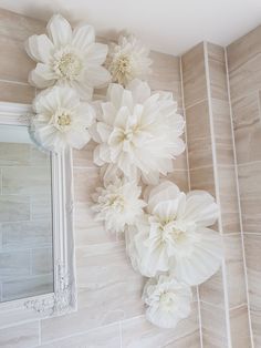 three white flowers are hanging on the wall next to a mirror