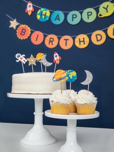 a birthday cake and cupcakes are sitting on pedestals in front of a blue wall