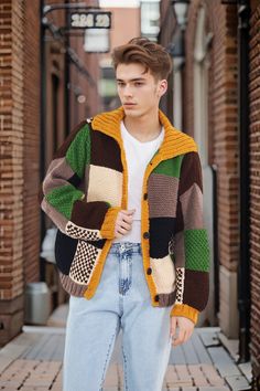 a young man is wearing a multicolored jacket and jeans while standing on the sidewalk