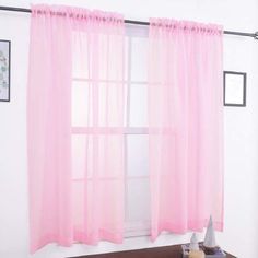 a window with pink sheer curtains hanging on it's side and a toy boat sitting in front of the window