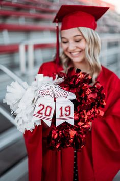 a woman wearing a red graduation gown and holding a pom - pom wreath