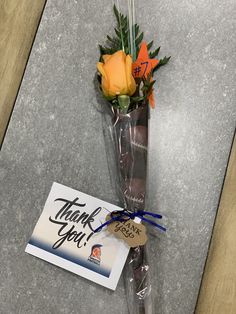 an orange rose in a clear vase with thank you tag